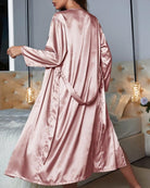 Vue de dos d’une femme portant le peignoir Calista en satin rose, longueur mi-mollet, avec ceinture à nouer à la taille. Peignoir fluide et élégant, idéal pour une allure chic et confortable à la maison.