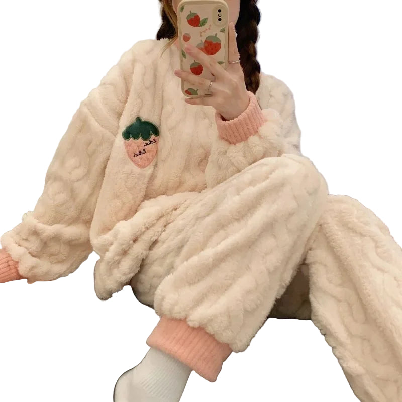 Pyjama femme beige en peluche, orné d'un motif de fraise sur le haut et le pantalon. Le haut présente des manches longues avec des bords roses, et le pantalon est également décoré de fraises et de rayures texturées. La personne porte le pyjama tout en prenant un selfie, créant une ambiance cosy, tendance et agréable.