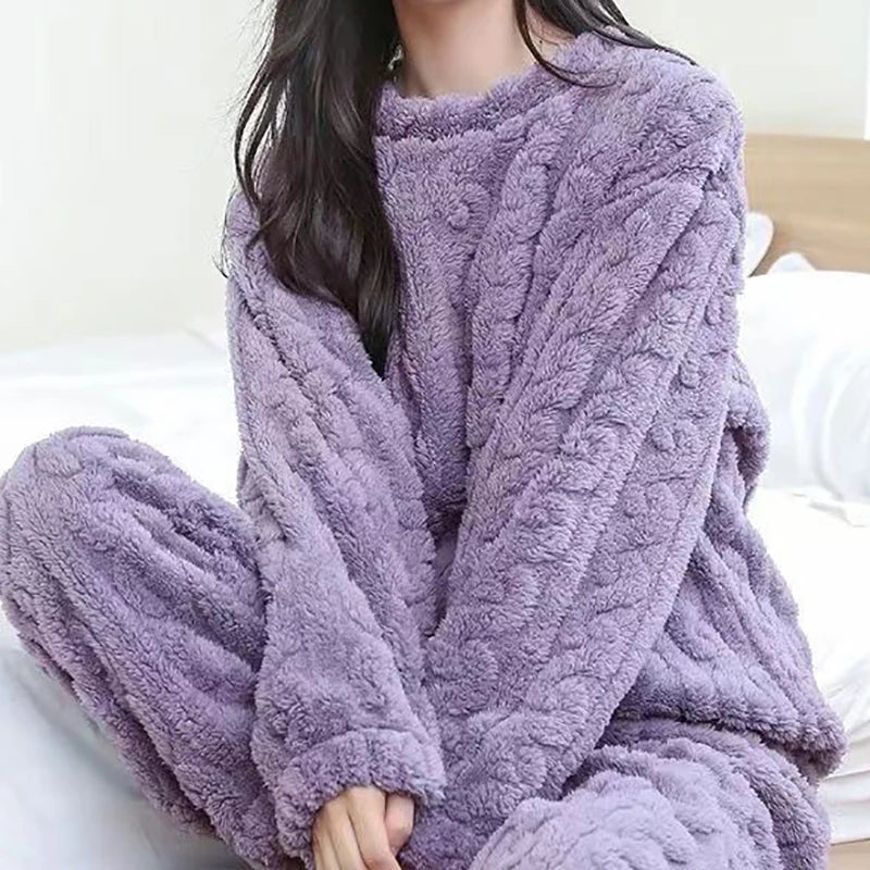 Femme assise confortablement sur un lit, portant le pyjama Camille en coloris lavande. Ensemble deux pièces en tissu peluche ultra doux à motif torsadé, idéal pour rester au chaud avec élégance. Un choix cosy, tendance et agréable pour vos soirées cocooning.