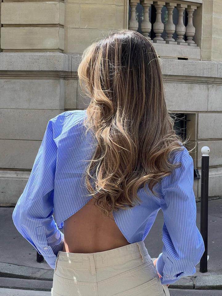 Vue arrière du chemisier rayé Carly pour femme, bleu clair, avec coupe courte et dos ouvert élégant, idéal pour un look estival léger et raffiné.