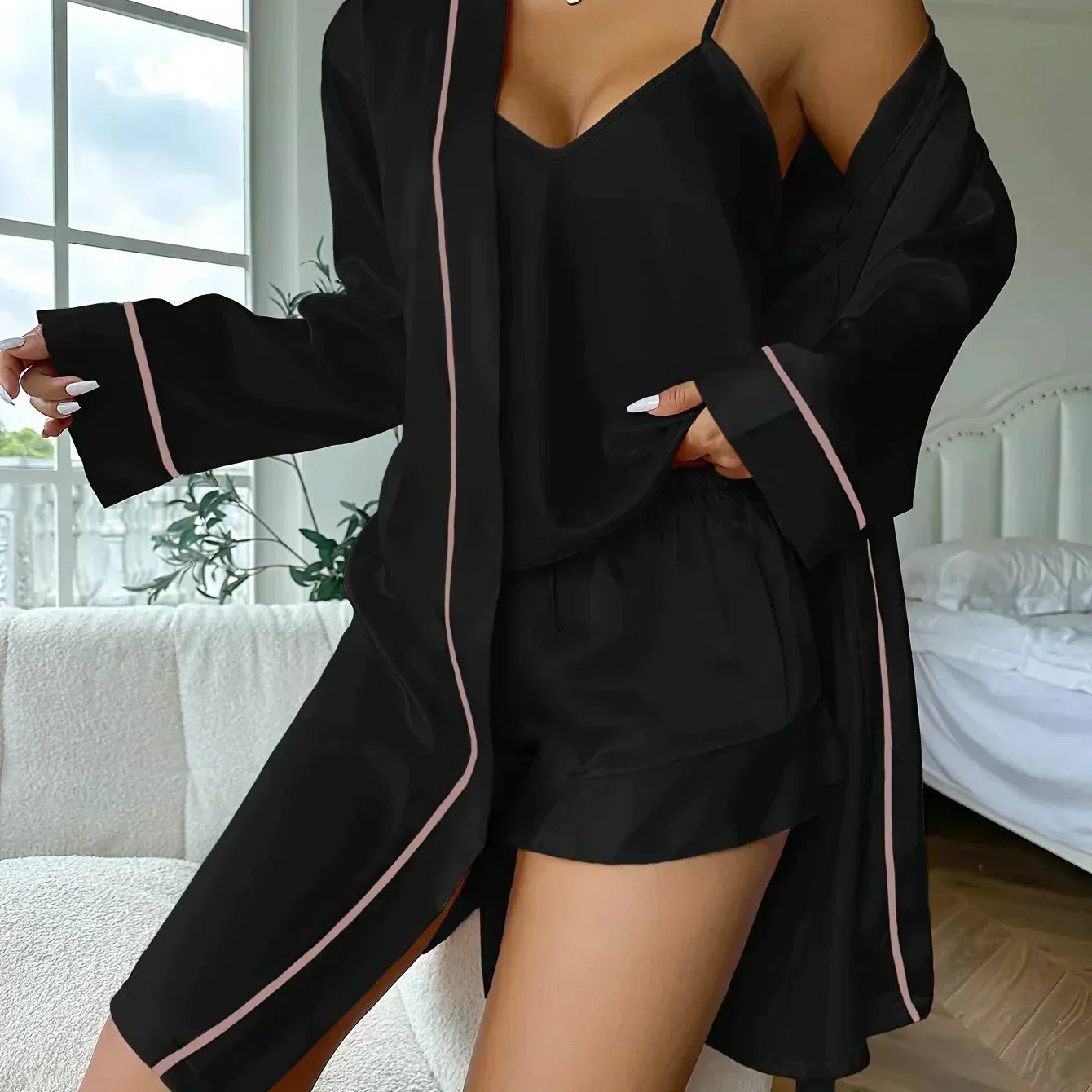 Pyjama satiné noir pour femme, comprenant un caraco à fines bretelles, un short fluide à taille élastique et une veste kimono assortie avec passepoils rose pâle. Ensemble chic et confortable, idéal pour des soirées relaxantes à la maison.
