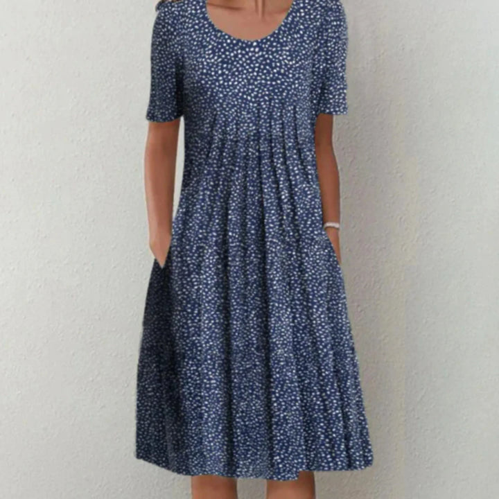 Robe midi femme Charlène légère et élégante, bleu marine à petits motifs blancs, manches courtes, encolure arrondie et coupe évasée avec poches, portée debout.