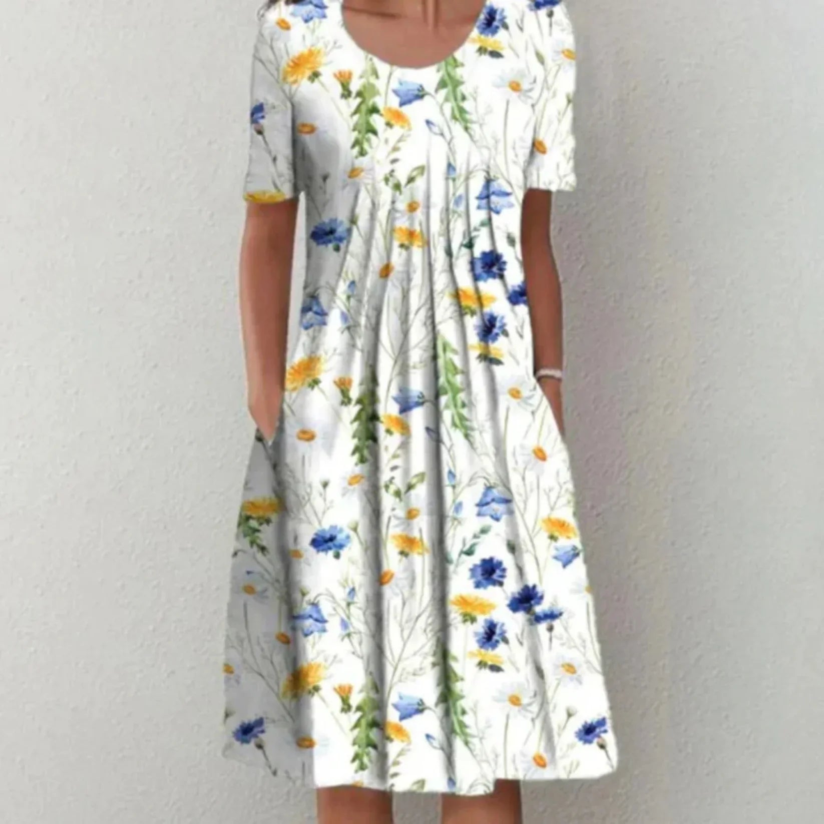 Robe midi femme Charlène légère et élégante, blanche à imprimé fleurs bleu et jaune, manches courtes, encolure arrondie et coupe évasée avec poches, portée debout.
