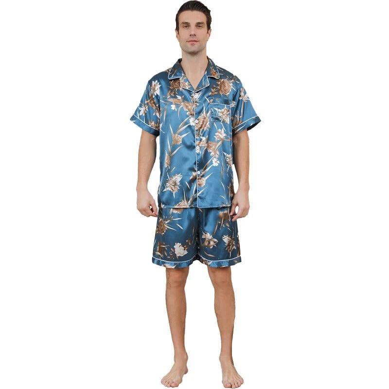 Homme portant le pyjama court satin Charles pour homme, ensemble deux pièces avec chemise boutonnée à manches courtes et short assorti, imprimé floral beige sur fond bleu, coupe droite, présenté sur fond blanc.