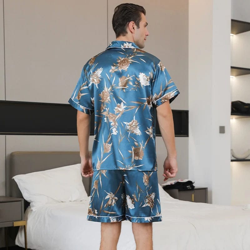 Vue arrière d’un homme portant le pyjama court satin Charles pour homme, ensemble deux pièces avec chemise à manches courtes et short assorti, imprimé floral beige sur fond bleu, coupe droite, présenté en intérieur.