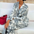 Gros plan du pyjama femme Charline gris imprimé toile de Jouy, chemise boutonnée à col tailleur et pantalon long assorti avec finitions passepoilées, tissu satiné élégant et confortable.