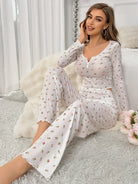 Pyjama floral femme Clarisse blanc, modèle assis au bord du lit portant un ensemble deux pièces doux et confortable avec haut à manches longues, col en V boutonné et bordures festonnées, pantalon large imprimé petites fleurs, coupe décontractée.
