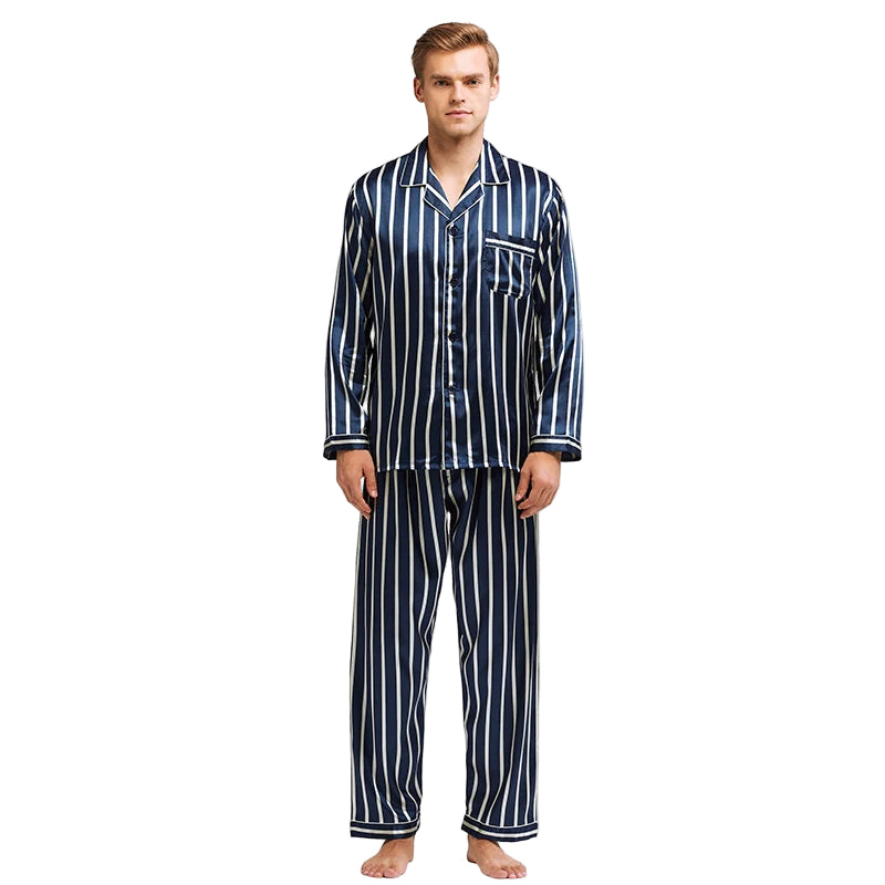 Homme debout portant un pyjama long en satin bleu marine à rayures verticales blanches, composé d’une chemise boutonnée avec poche poitrine et d’un pantalon assorti. Ensemble élégant et confortable, parfait pour des nuits stylées ou la détente à la maison.