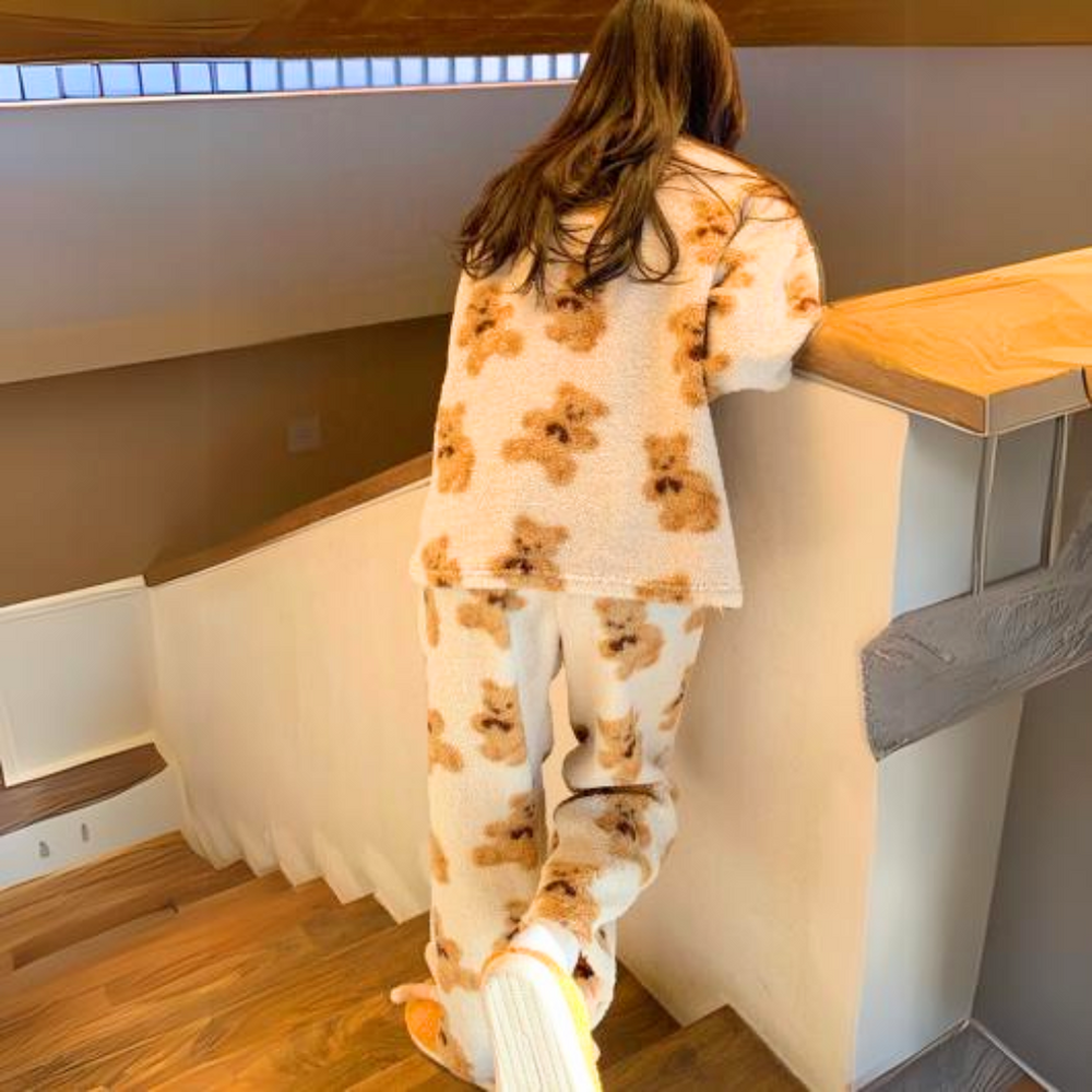 Femme assise dans un fauteuil, portant un pyjama polaire crème à motifs oursons marron, composé d’un haut à manches longues et d’un pantalon assorti. Ensemble ultra doux et moelleux, parfait pour l’hiver et les moments cocooning à la maison.