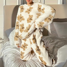 Femme debout sur un lit, vêtue du pyjama polaire Colette en blanc crème avec motifs oursons marron, composé d’un haut ample à manches longues et d’un pantalon assorti. Ensemble ultra doux et agréable, parfait pour cocooner au chaud avec style.