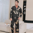 Homme portant le pyjama satin homme Corentin noir à motifs dorés, ensemble élégant et confortable avec chemise boutonnée et pantalon long, présenté dans un intérieur moderne.