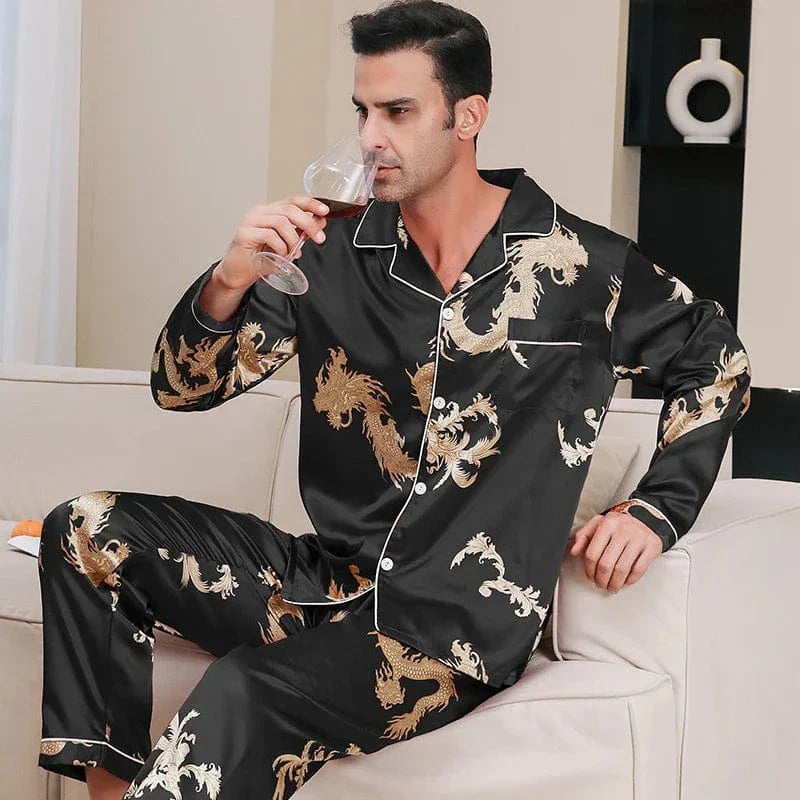 Homme portant le pyjama satin homme Corentin noir à motifs dragon dorés, assis sur un canapé, chemise boutonnée à col classique et pantalon long, style élégant et confortable pour la maison.