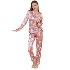 Femme portant un pyjama en satin rose orné de motifs cœurs blancs et d'inscriptions romantiques. Ensemble deux pièces avec chemise à manches longues boutonnée et pantalon assorti. Pyjama tendance, doux au toucher et agréable à porter, parfait pour des nuits stylées et confortables.