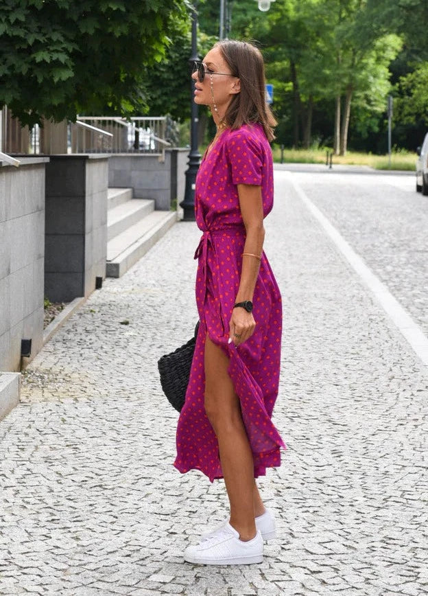 Robe midi à imprimé fuchsia à pois, avec une coupe fluide et une fente sur le côté, cintrée à la taille avec une ceinture. Portée avec des baskets blanches pour un look chic et décontracté, parfaite pour les journées estivales.