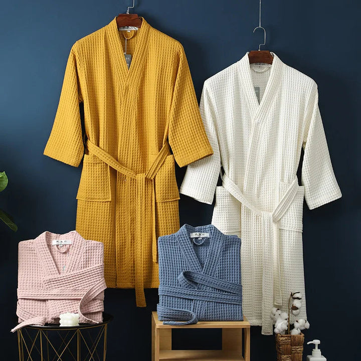 Collection de peignoirs Damien pour homme, modèles moelleux et confortables en tissu gaufré, présentés suspendus ou pliés dans plusieurs couleurs : jaune moutarde, blanc, rose poudré et bleu, avec accessoires de salle de bain en décor.
