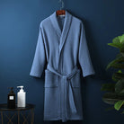 Peignoir Damien pour homme, modèle moelleux et confortable en tissu gaufré bleu, présenté suspendu devant un mur bleu avec accessoires de salle de bain en décor.