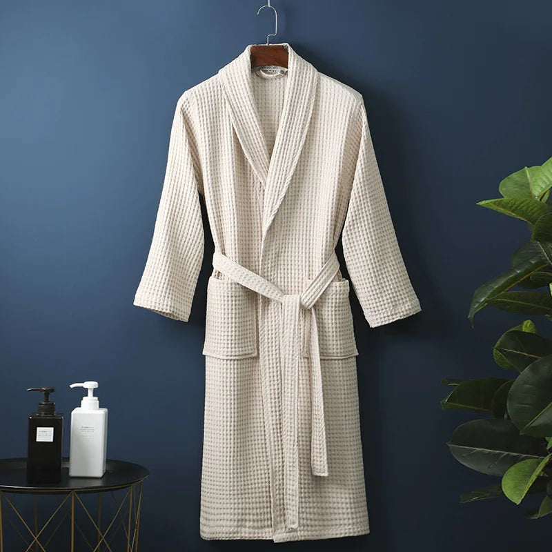 Peignoir Damien pour homme, modèle moelleux et confortable en tissu gaufré beige, présenté suspendu devant un mur bleu avec accessoires de salle de bain en décor.