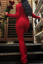 Femme montant un escalier, vue de dos, portant l’ensemble Dani en maille rouge vif, composé d’un haut ajusté à manches longues et d’un pantalon taille haute assorti. Tenue élégante, féminine et confortable, parfaite pour un look chic en intérieur ou pour une occasion spéciale.
