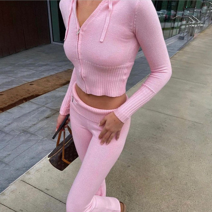 Femme marchant en extérieur, vêtue de l’ensemble Dani en maille rose clair, composé d’un haut zippé court à capuche et manches longues, et d’un pantalon taille haute assorti. Tenue féminine, douce et élégante, parfaite pour un look tendance et confortable en ville.