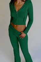 Femme portant l’ensemble Dani en maille verte, composé d’un haut court à capuche zippé et manches longues, et d’un pantalon taille basse avec ceinture intégrée. Tenue près du corps, élégante et confortable, idéale pour un look moderne et affirmé.