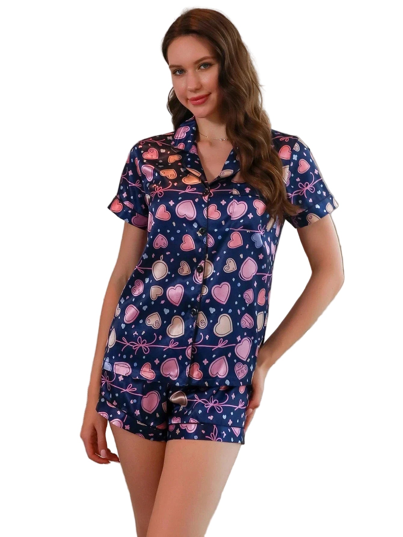Femme portant un pyjama court en satin bleu marine imprimé de cœurs roses et beiges. Le haut boutonné à manches courtes est assorti à un short fluide. Tenue légère, douce et confortable, idéale pour les nuits d’été et les instants cocooning avec une touche girly.