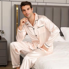 Pyjama satin homme couleur rose pâle, élégant et confortable, avec une chemise à boutons, une poche sur la poitrine et des finitions noires, accompagnée d'un pantalon assorti pour un confort optimal pendant la nuit.