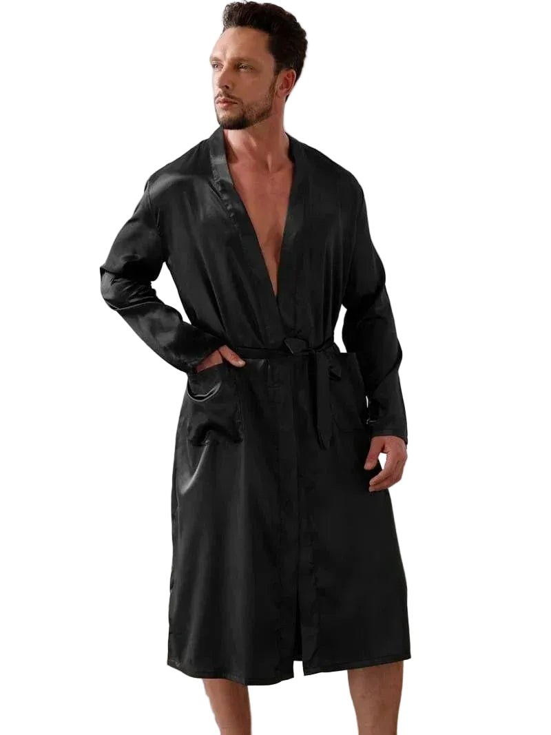 Homme portant un kimono en satin noir pour homme Dorian, avec ceinture assortie, manches longues et coupe raffinée, présenté dans un intérieur lumineux au style moderne.