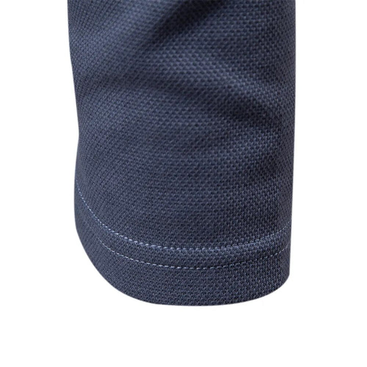 Détail du bas de la manche du polo bleu, mettant en valeur la finition soignée avec un bord côtelé et une texture subtile. Un design élégant et moderne qui assure confort et durabilité.