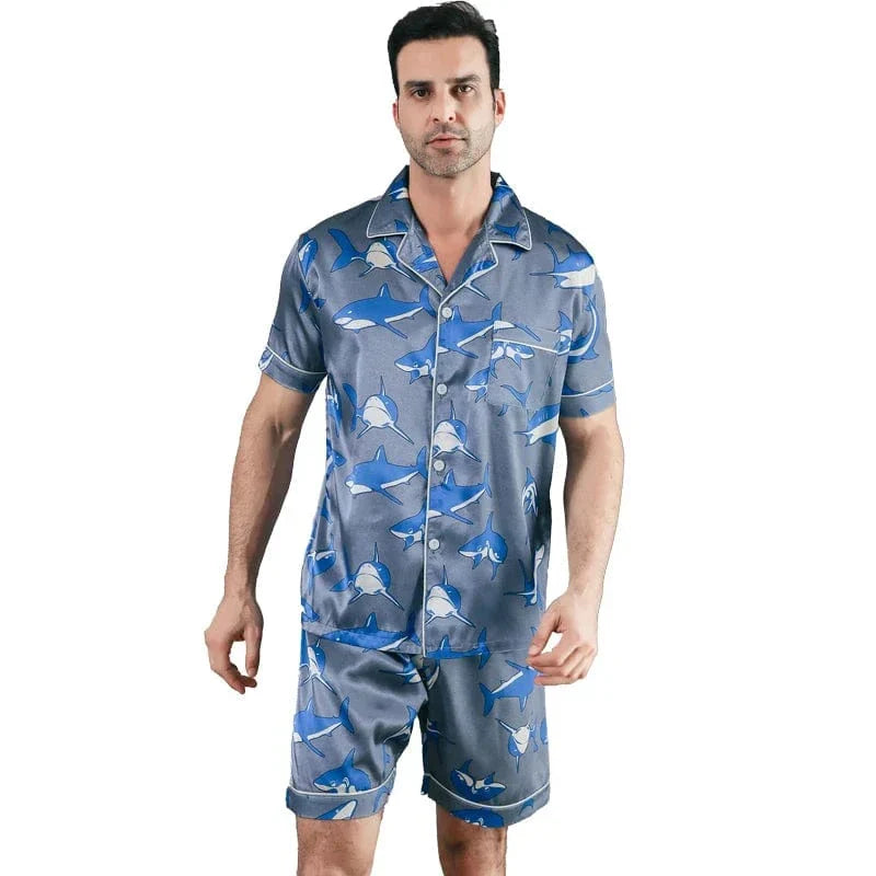 Homme debout portant le shorty satin pour homme Edouard, ensemble tendance et confortable composé d’une chemise à manches courtes boutonnée et d’un short assorti, en satin gris-bleu à imprimé requins, avec finitions soignées pour un style moderne et un confort idéal à la maison ou pour la nuit.