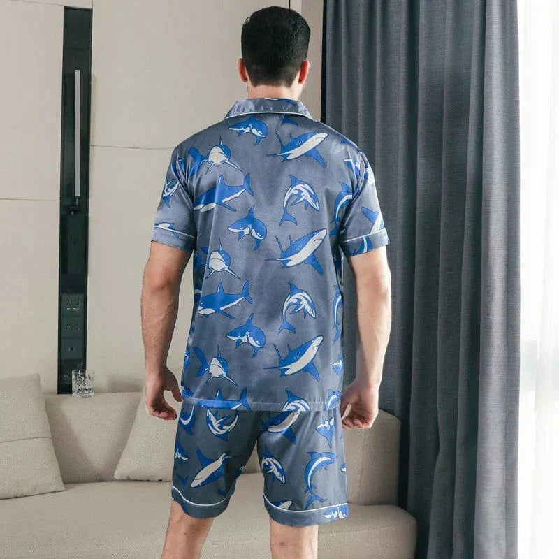 Vue de dos d’un homme portant le shorty satin pour homme Edouard, ensemble tendance et confortable composé d’une chemise à manches courtes et d’un short assorti, en satin gris-bleu à imprimé requins, offrant une coupe soignée et un style moderne idéal pour la maison ou la nuit.