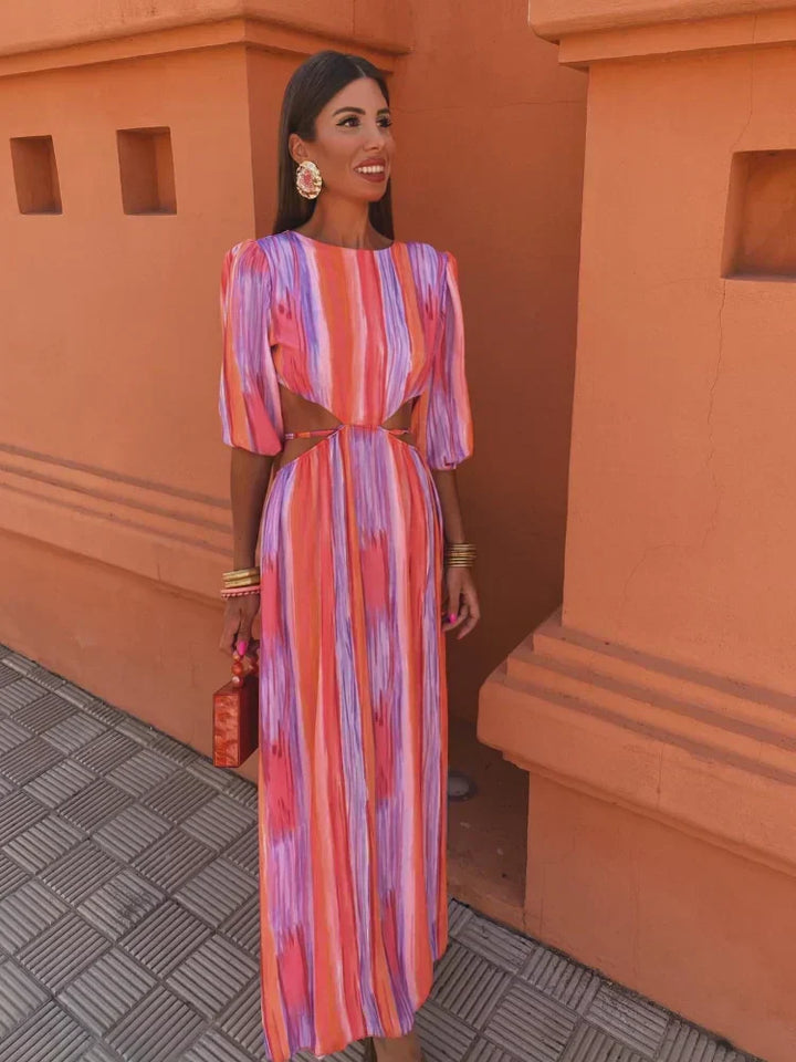 Modèle porteur de la robe maxi tie-dye pour femme, mettant en valeur le design coloré avec des teintes vibrantes de rose, violet et orange. Les manches bouffantes et les découpes latérales ajoutent une touche de modernité et de fraîcheur, idéale pour les journées estivales.