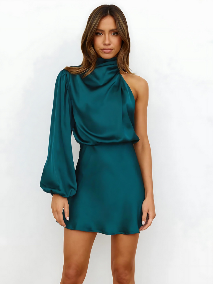 Modèle portant la robe mini Elia en satin asymétrique, dans une teinte bleu sarcelle élégante. La robe met en valeur la silhouette avec sa coupe moderne et une manche longue, offrant une allure sophistiquée et tendance. Idéale pour des occasions spéciales, elle combine confort et élégance.