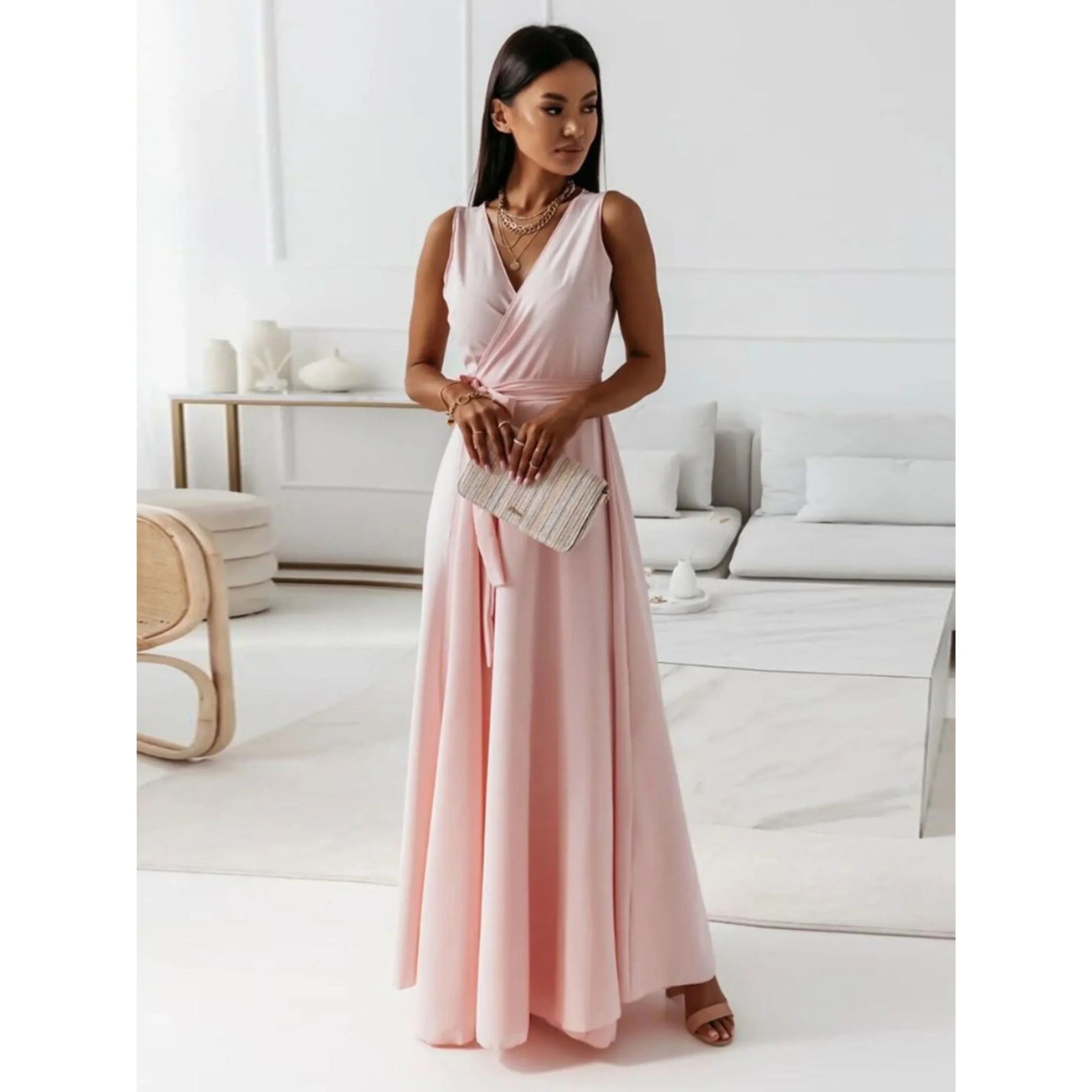 Rose poudré, décolleté en V croisé, taille ceinturée et jupe fluide, avec sandales et pochette, dans un intérieur lumineux.