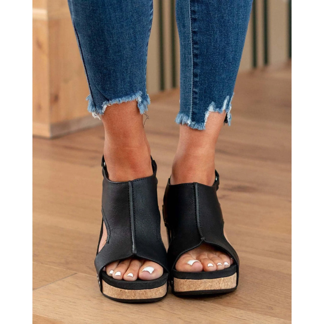 Sandales en cuir noires Elodine pour femmes avec plateforme en liège, portées avec un jean déchiré aux chevilles.