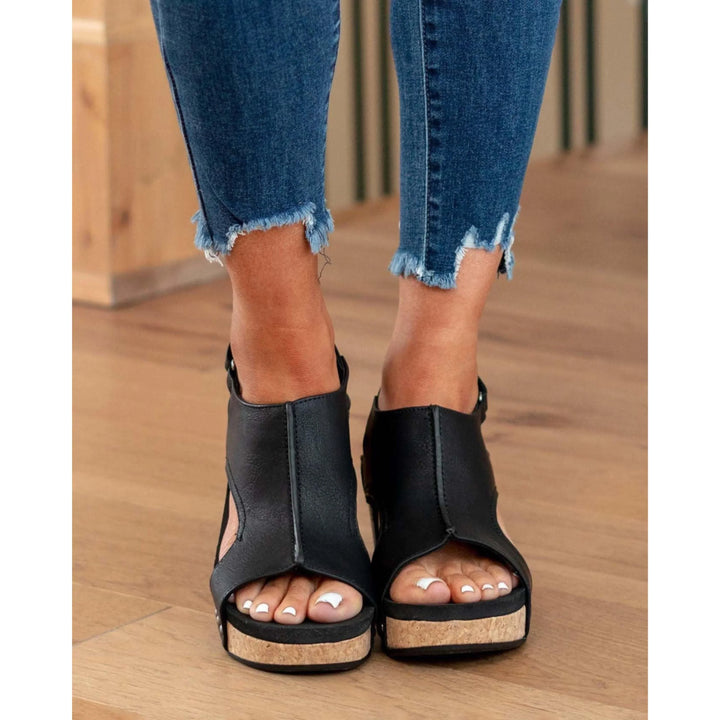 Sandales en cuir noires Elodine pour femmes avec plateforme en liège, portées avec un jean déchiré aux chevilles.