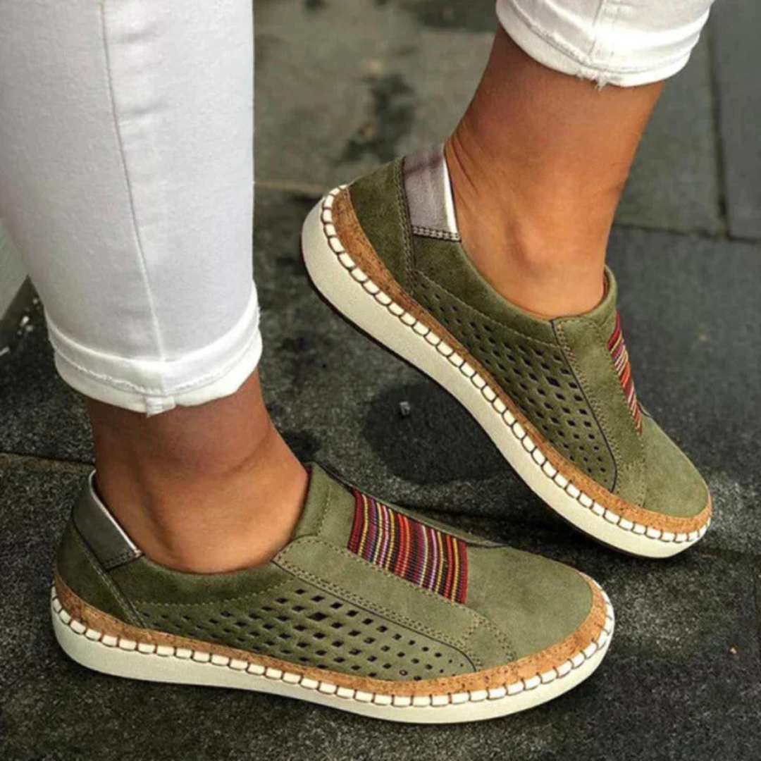 Chaussures femme confortables et idéales au quotidien, slip-on kaki avec bande rayée, perforations respirantes et semelle épaisse beige effet liège, portées avec un pantalon blanc.