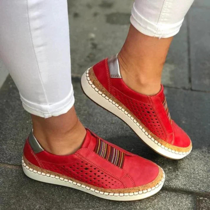 Chaussures femme confortables et idéales au quotidien, slip-on rouges avec bande rayée, perforations respirantes et semelle épaisse beige effet liège, portées avec un pantalon blanc.
