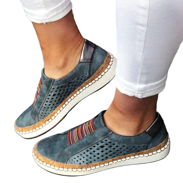 Chaussures femme confortables et idéales au quotidien, slip-on bleu denim avec empiècement rayé, perforations respirantes et semelle épaisse blanche, portées avec un pantalon blanc.