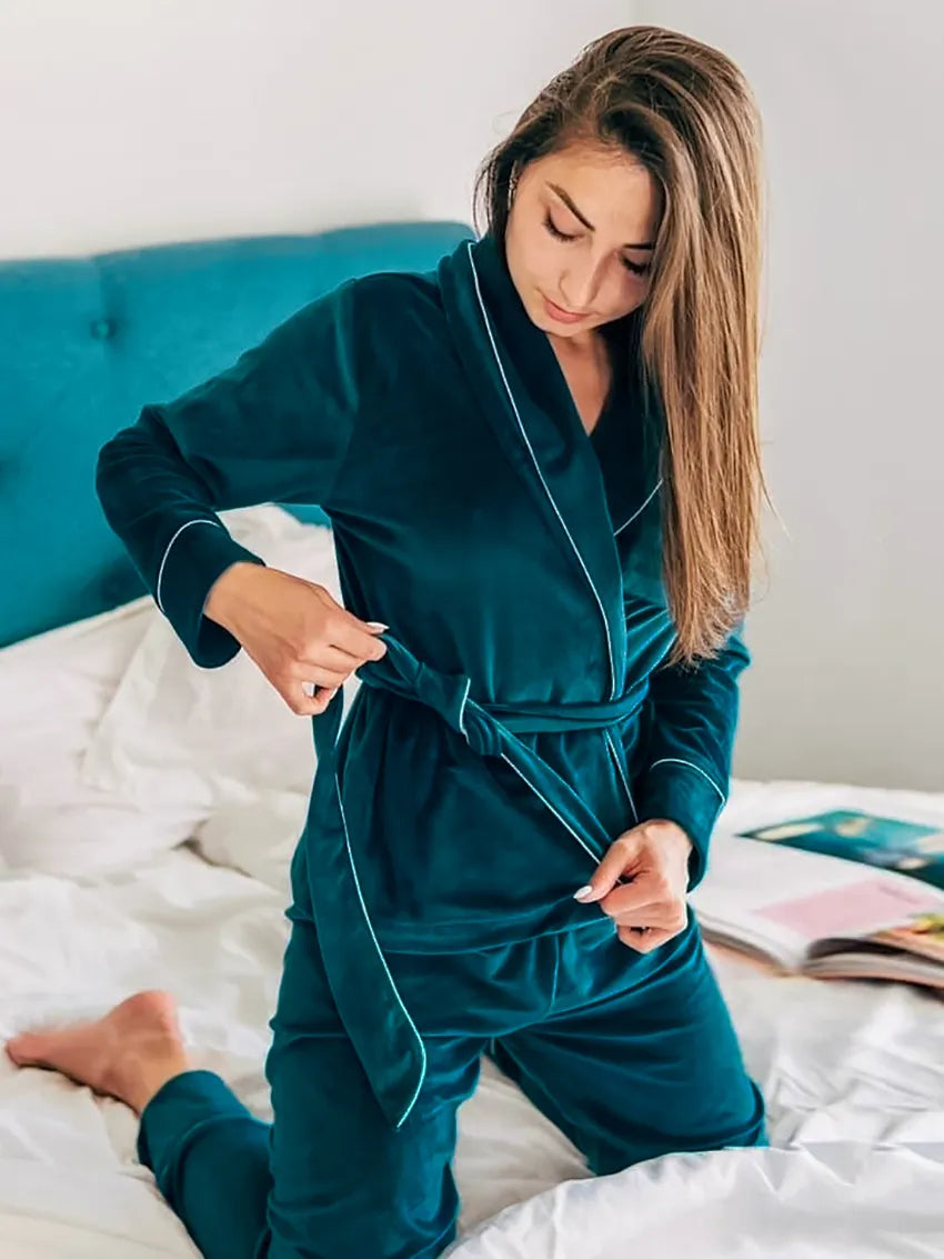Femme à genoux sur un lit portant un pyjama en velours vert foncé composé d’une veste croisée à ceinture et d’un pantalon assorti. Ensemble chaud, doux et très confortable, idéal pour l’hiver et les moments cocooning à la maison.