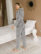 Femme debout dans une chambre, portant un pyjama en velours gris composé d’une veste à ceinture et d’un pantalon assorti. Ensemble chaud, doux et très confortable, idéal pour l’hiver et les moments de détente à la maison.