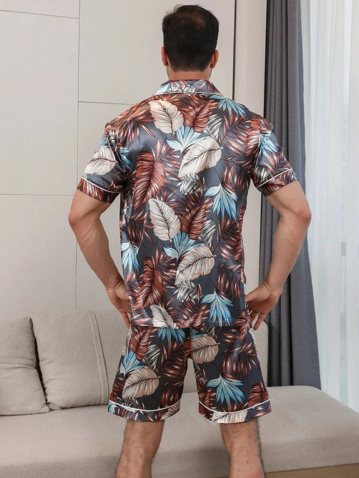 Vue arrière d’un homme portant le pyjama satin Enzo pour homme, ensemble deux pièces avec chemise à manches courtes et short assorti, imprimé feuillage multicolore, coupe droite, présenté en intérieur.