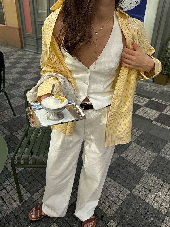 Chemise rayée Ever pour femme, jaune à fines rayures, élégante et polyvalente, portée ouverte sur une tenue blanche pour un look chic et décontracté en été.