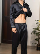 Homme portant un pyjama noir en satin avec chemise boutonnée à passepoils blancs et pantalon long assorti, dévoilant son abdomen pour montrer le confort et la légèreté du tissu. Ensemble doux, élégant et agréable à porter pour la nuit ou la détente à la maison.