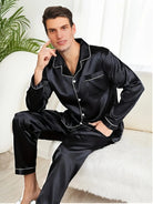 Homme assis sur un canapé, portant un pyjama noir en satin avec chemise boutonnée à col et passepoils blancs, accompagné d’un pantalon assorti. Ensemble élégant, doux et confortable, idéal pour les soirées relax et le sommeil tout en style.