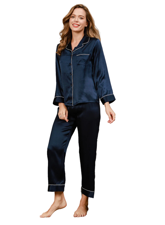 Femme souriante portant le pyjama Felicity, ensemble deux pièces en satin bleu marine avec passepoils contrastants blancs. Pyjama doux, élégant et confortable, idéal pour des nuits stylées ou des moments de détente à la maison.