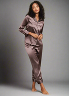 Femme debout portant le pyjama Felicity en satin chocolat brillant avec passepoils contrastés. Ensemble deux pièces élégant et confortable, composé d’une chemise boutonnée à manches longues et d’un pantalon fluide, idéal pour des nuits raffinées et relaxantes.
