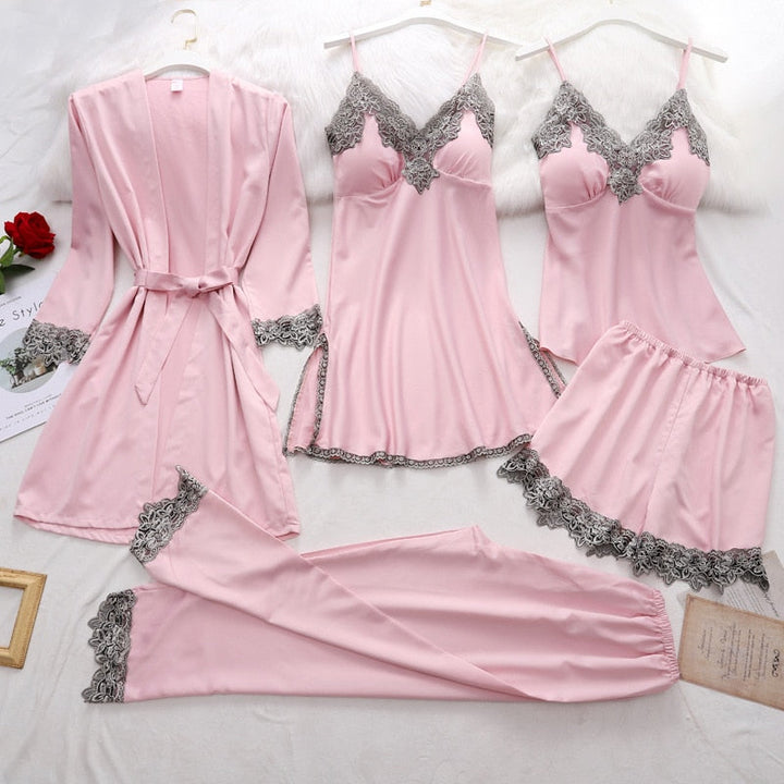 Ensemble de nuit pour femme en satin rose clair avec finitions en dentelle assortie, comprenant six pièces : un kimono ceinturé, une nuisette à bretelles fines, un débardeur, un short, un pantalon long et une culotte (hors cadre). Design raffiné et confortable, parfait pour allier élégance et douceur lors des soirées à la maison.