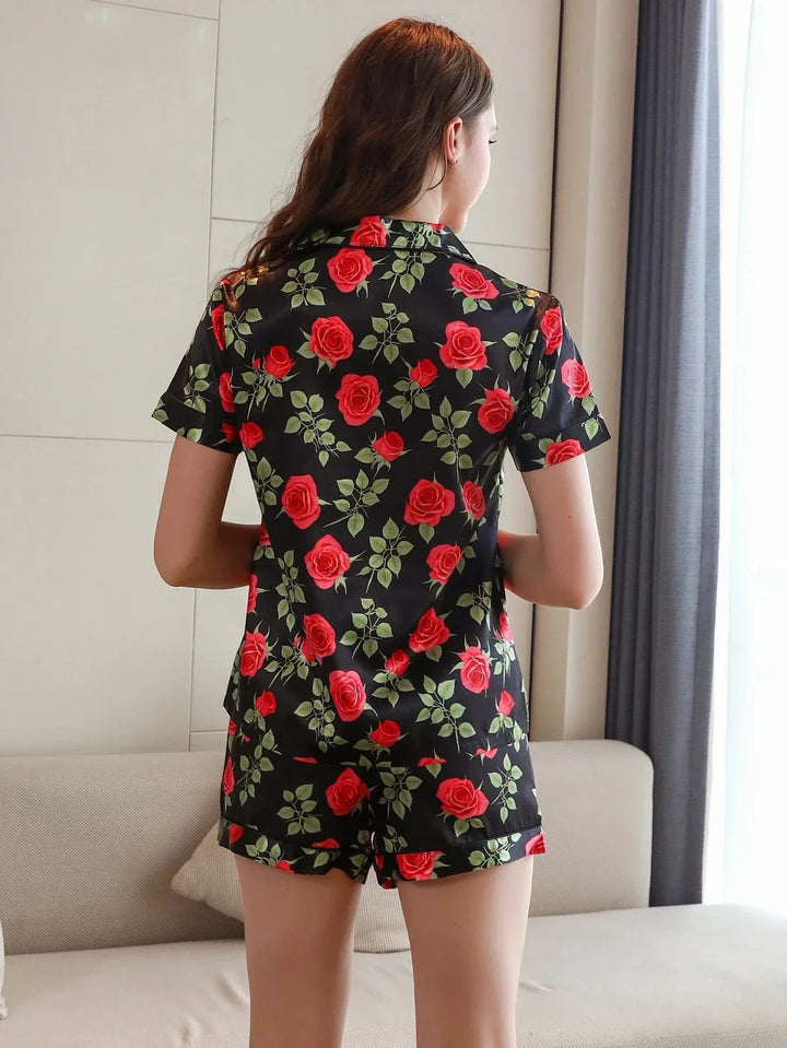 Femme vue de dos portant le pyjama short femme, un ensemble léger et élégant parfait pour l’été, composé d’une chemise à manches courtes et d’un short assorti en satin noir décoré d’un imprimé de roses rouges et de feuilles vertes.