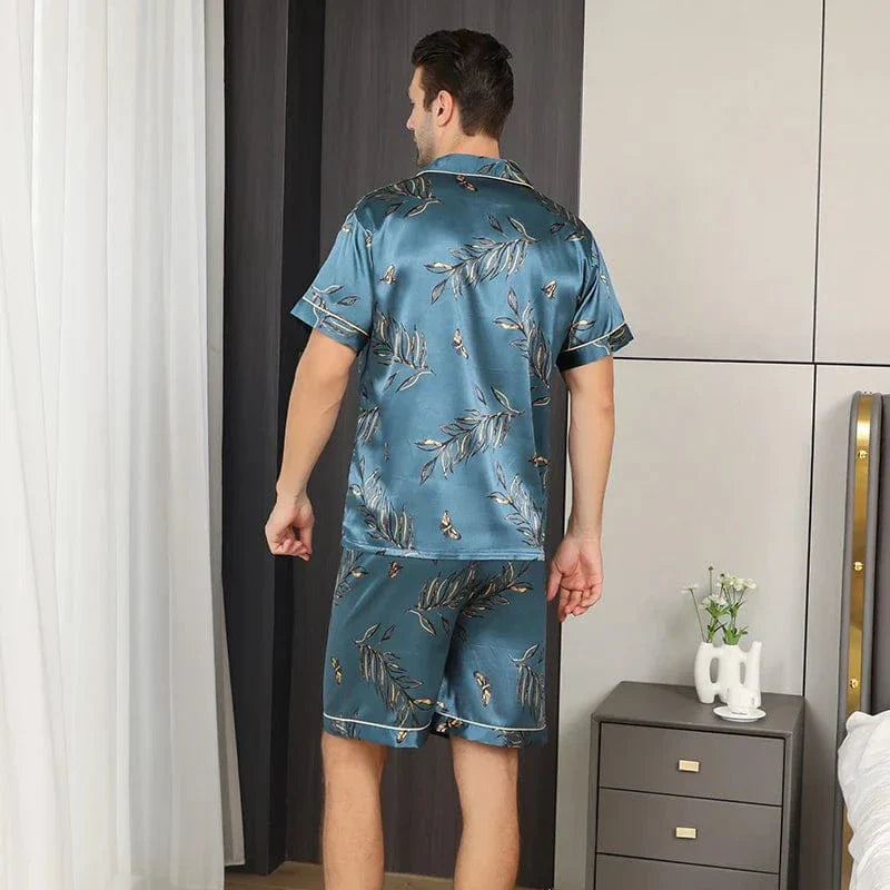 Vue arrière d’un homme portant le shorty satin François pour homme, ensemble deux pièces avec chemise à manches courtes et short assorti, imprimé feuillage sur fond bleu-vert, coupe droite, présenté en intérieur.