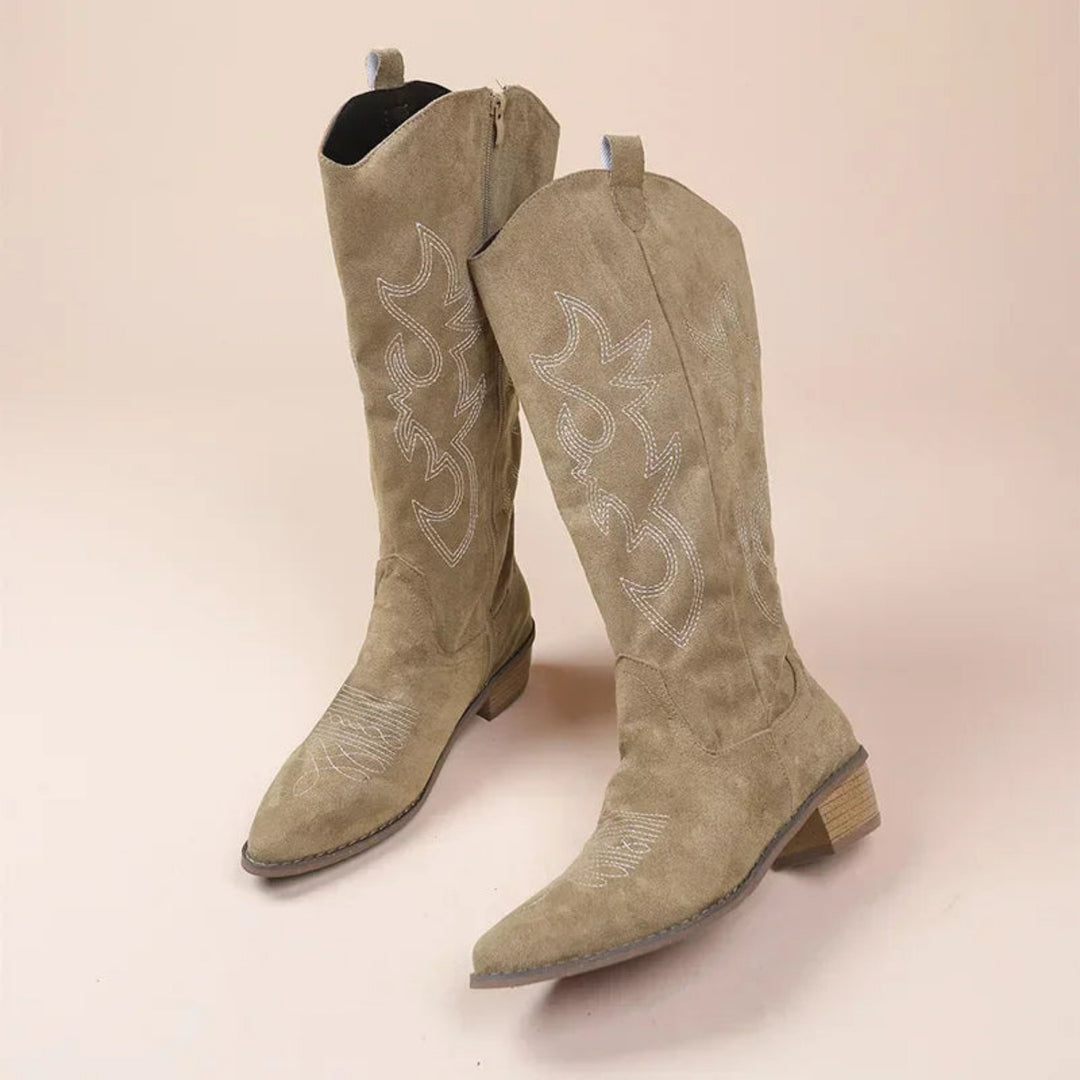 Paire de bottes western en suédine beige/sable, tige haute avec surpiqûres décoratives, bout pointu et talon bas, vue en angle.
